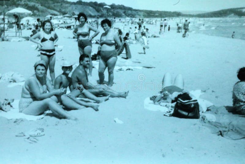 Vintage black and white photo of a people on a beach enjoying the sun, wearing swimming costumes / trunks. Men and women, family, friends, holiday 1950s fashion. Social history. Vintage black and white photo of a people on a beach enjoying the sun, wearing swimming costumes / trunks. Men and women, family, friends, holiday 1950s fashion. Social history.